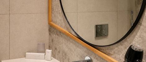 A modern bathroom with a white sink, a round mirror with a wooden frame, and a hairdryer mounted on the wall.
