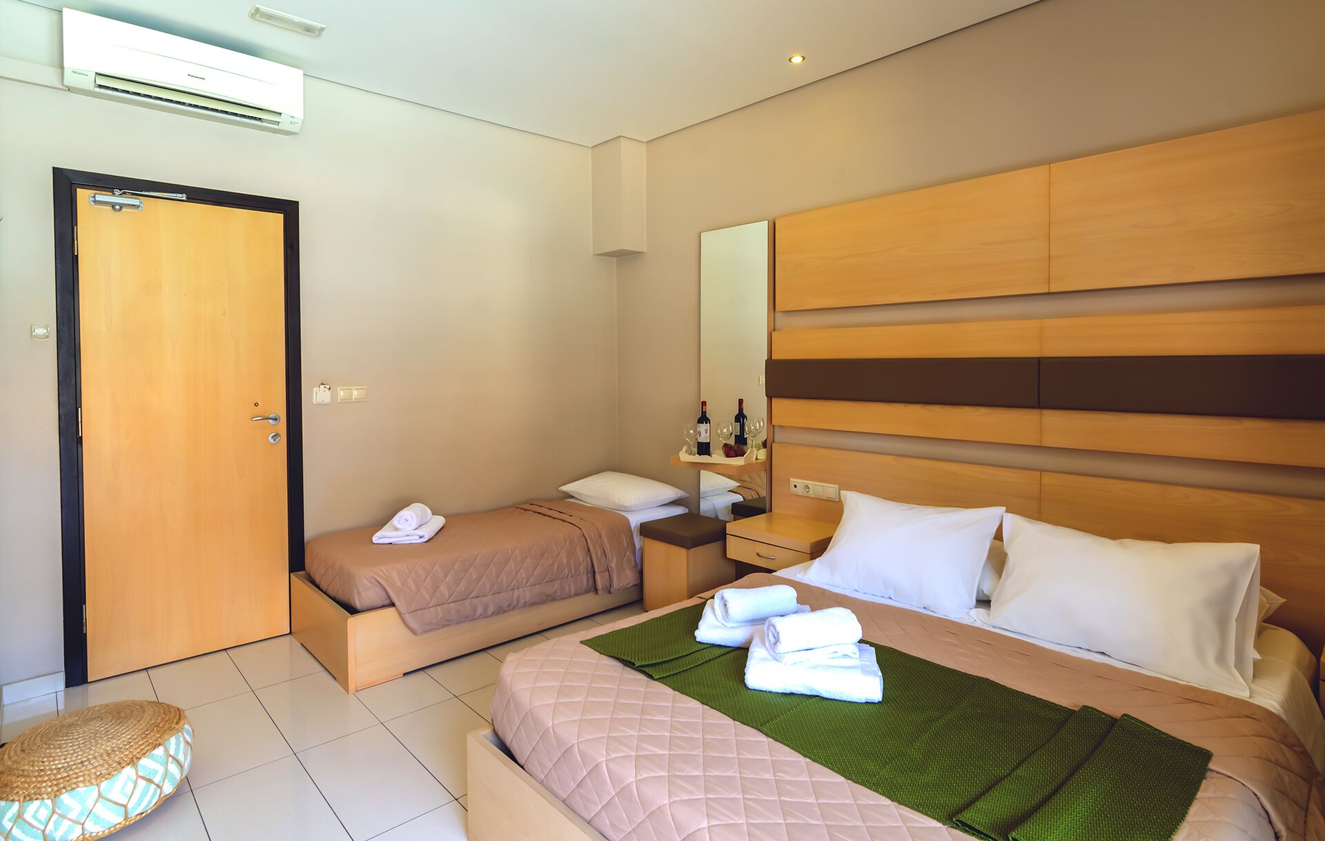 Habitación de hotel con dos camas, cabecera de madera, mesita de noche con espejo y un pequeño rincón de descanso.