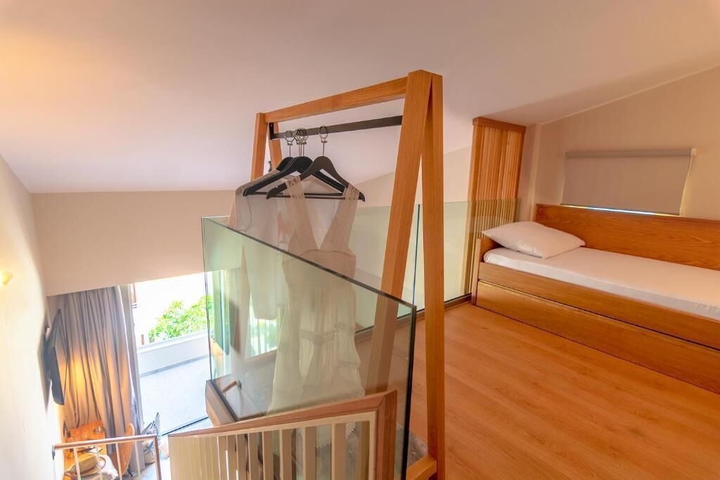 Une chambre dotée d’un balcon en verre, d’un lit en bois et d’un porte-vêtements suspendu.