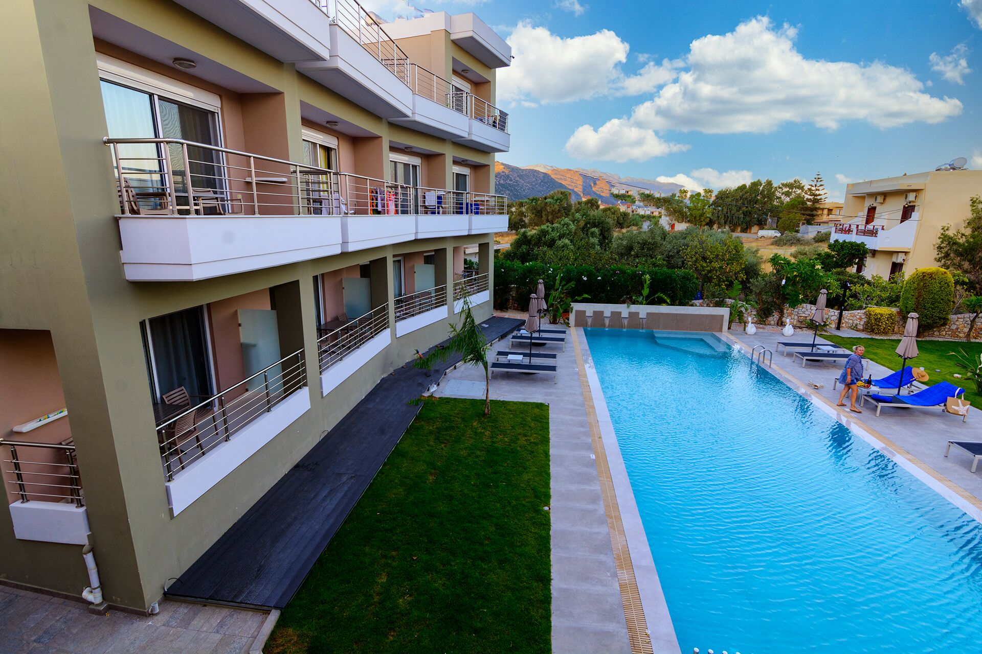 A modern hotel with a swimming pool, balconies, and a view of the mountains.