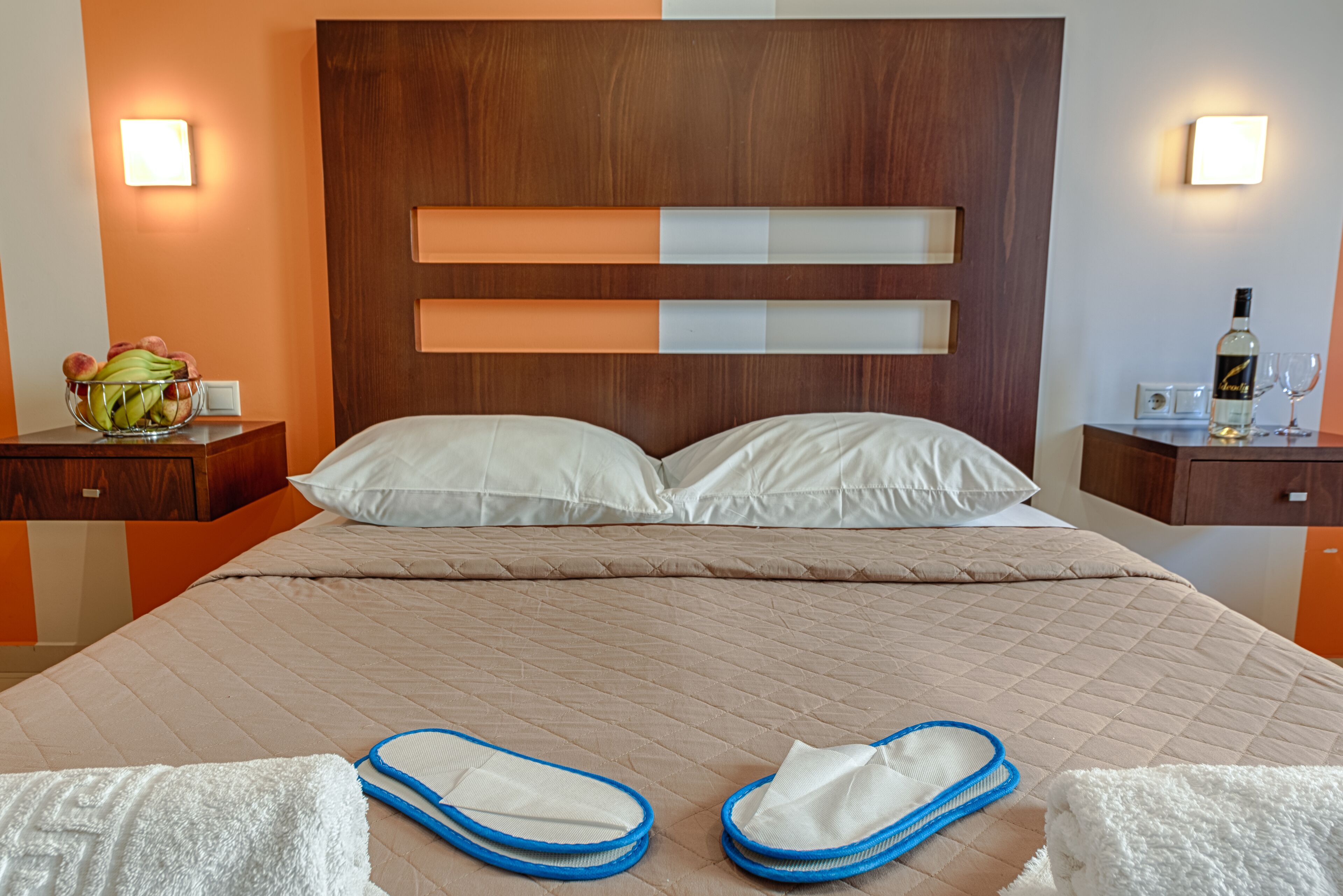 Habitación de hotel con una cama grande, dos mesitas de noche, un cabecero de madera y una lámpara de pared.