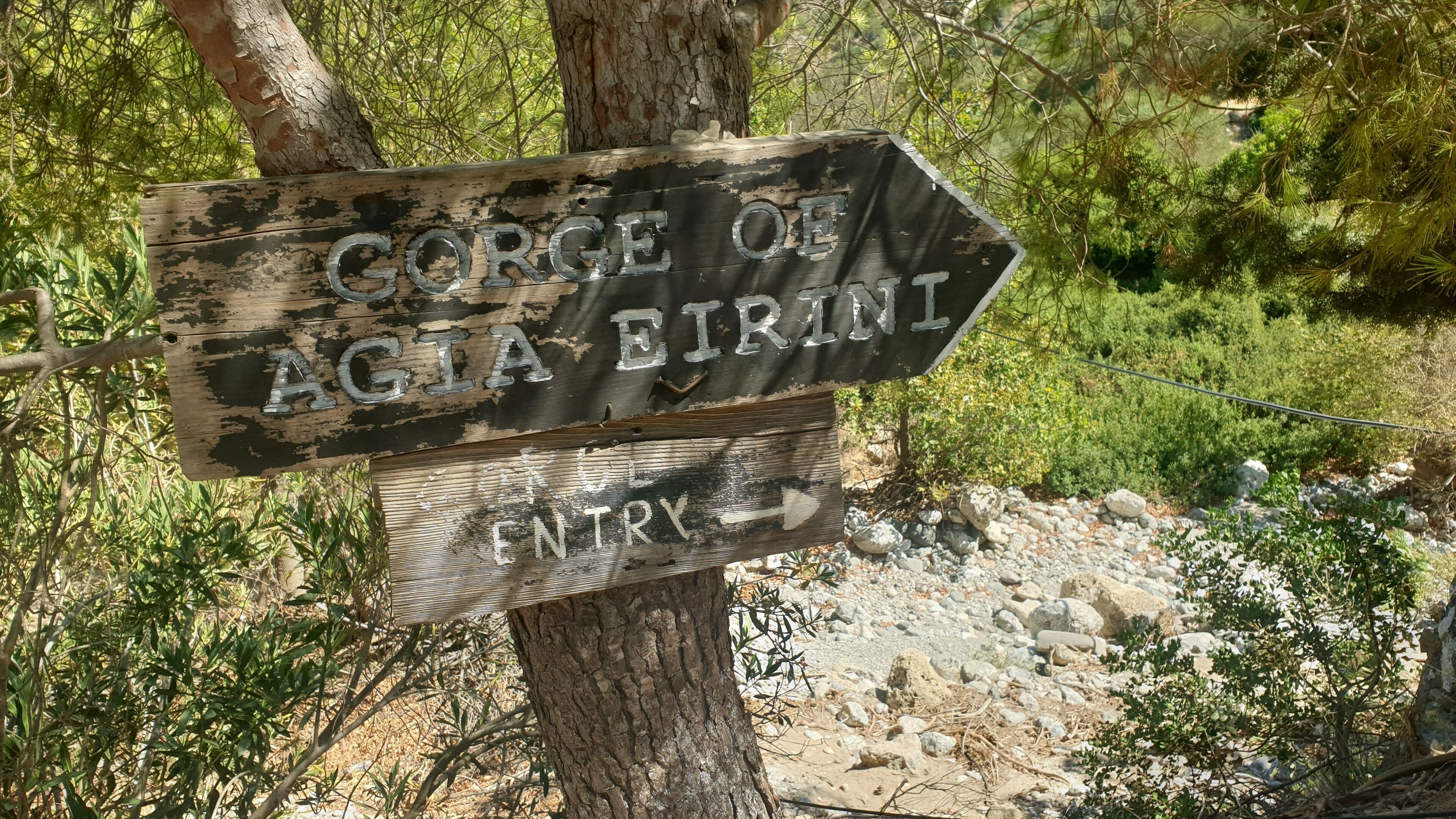 Un cartel de madera con el texto 'Gorge of Agia Eirini' y una flecha señalando a la derecha, indicando un sendero o entrada.