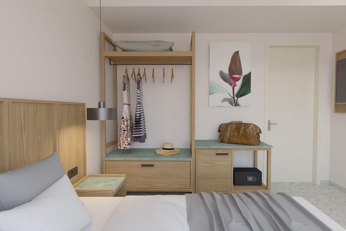 Ein Hotelzimmer mit Bett, Schreibtisch mit Stuhl, Kleiderschrank, Nachttisch, Lampe und Fernseher.