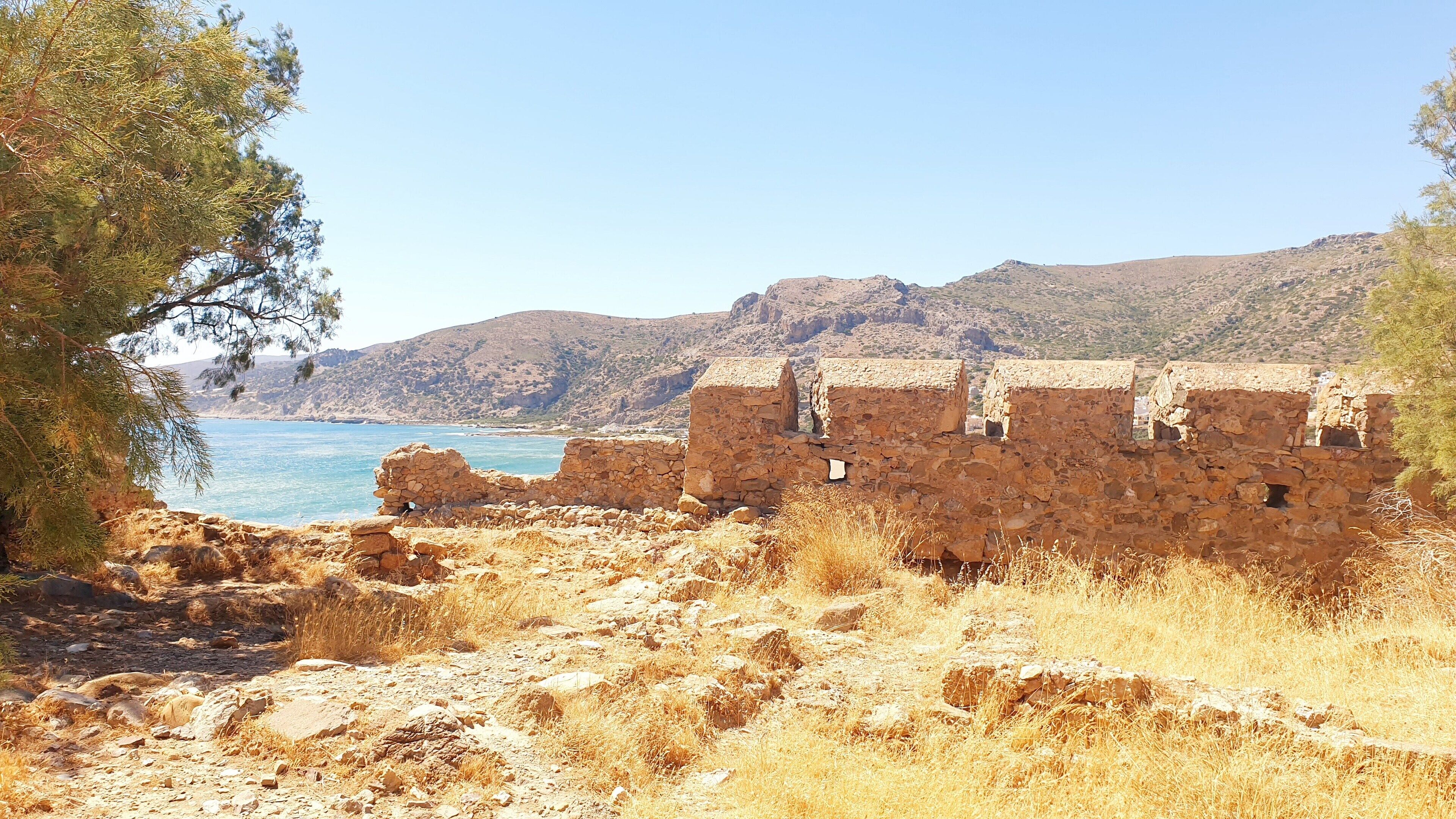 A coastal stone structure with a view of the sea and hills.