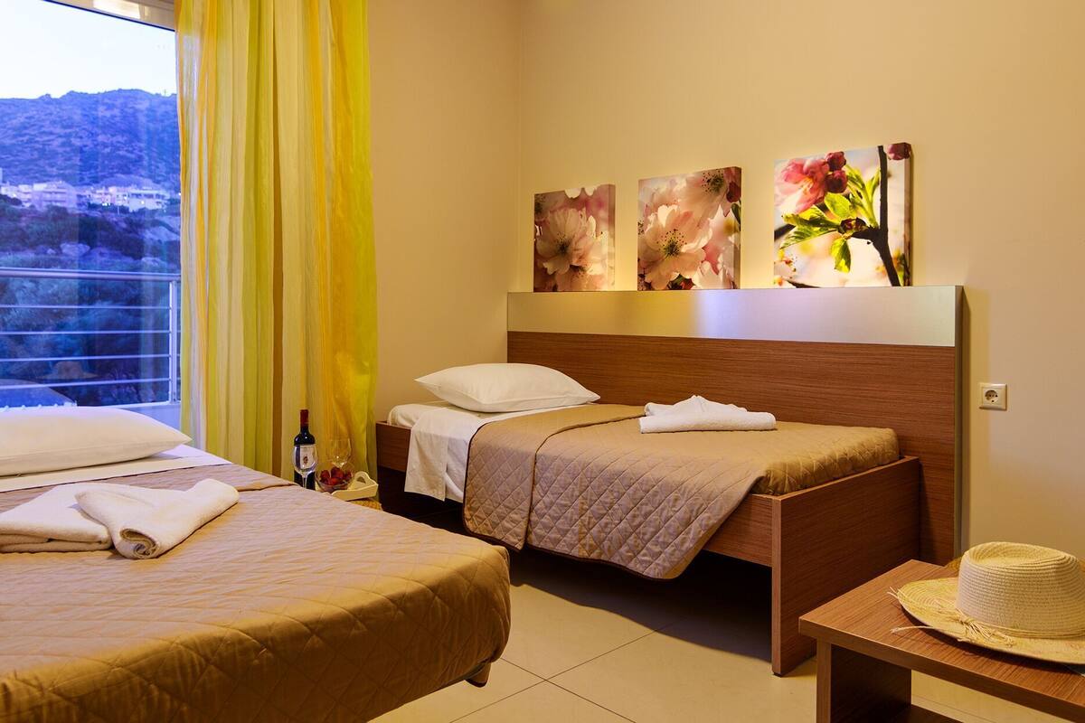 Une chambre d’hôtel avec deux lits, une fenêtre donnant sur des collines et des œuvres d’art accrochées au mur.