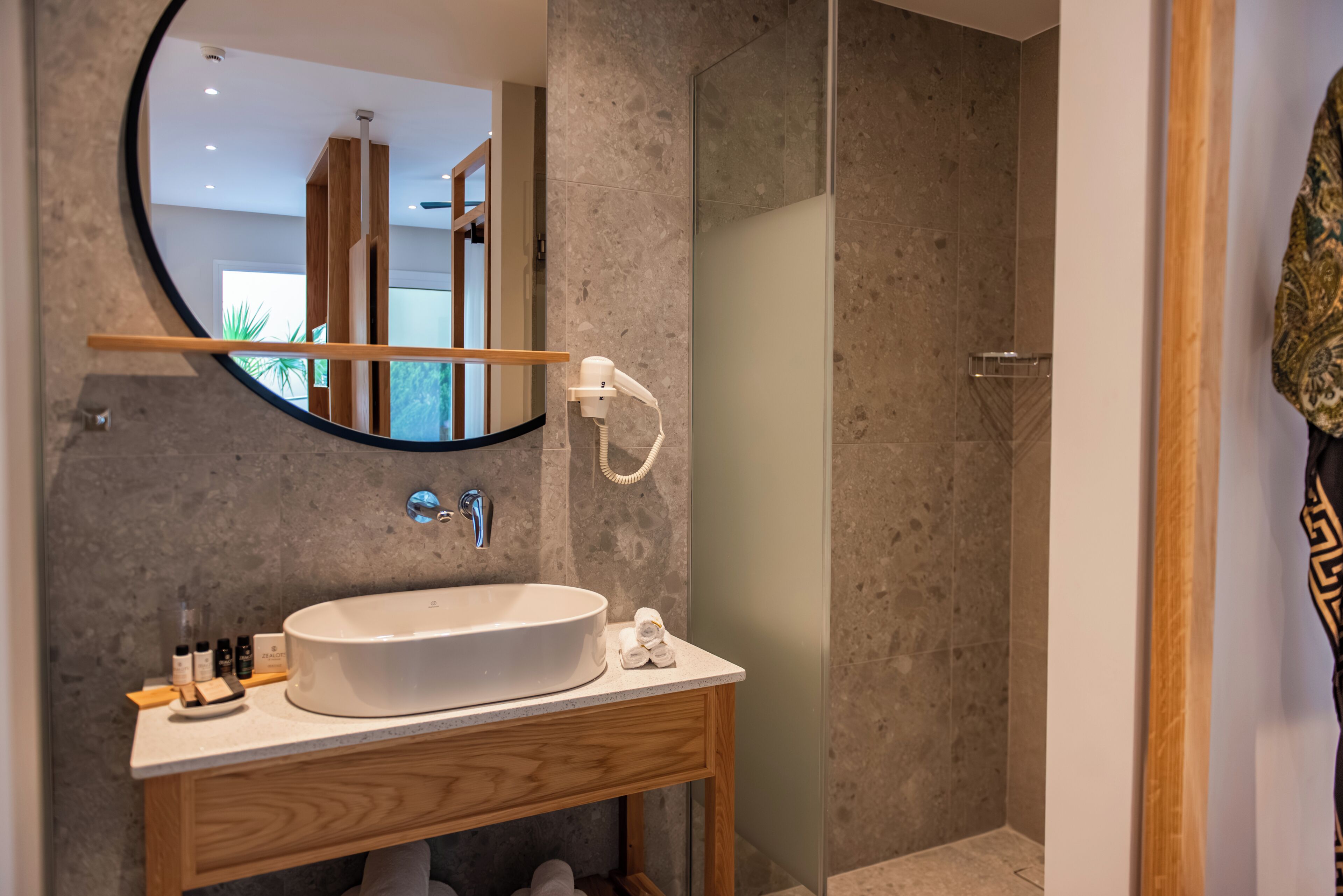Un baño moderno con un lavamanos independiente, un espejo redondo y una cabina de ducha con paredes de vidrio.