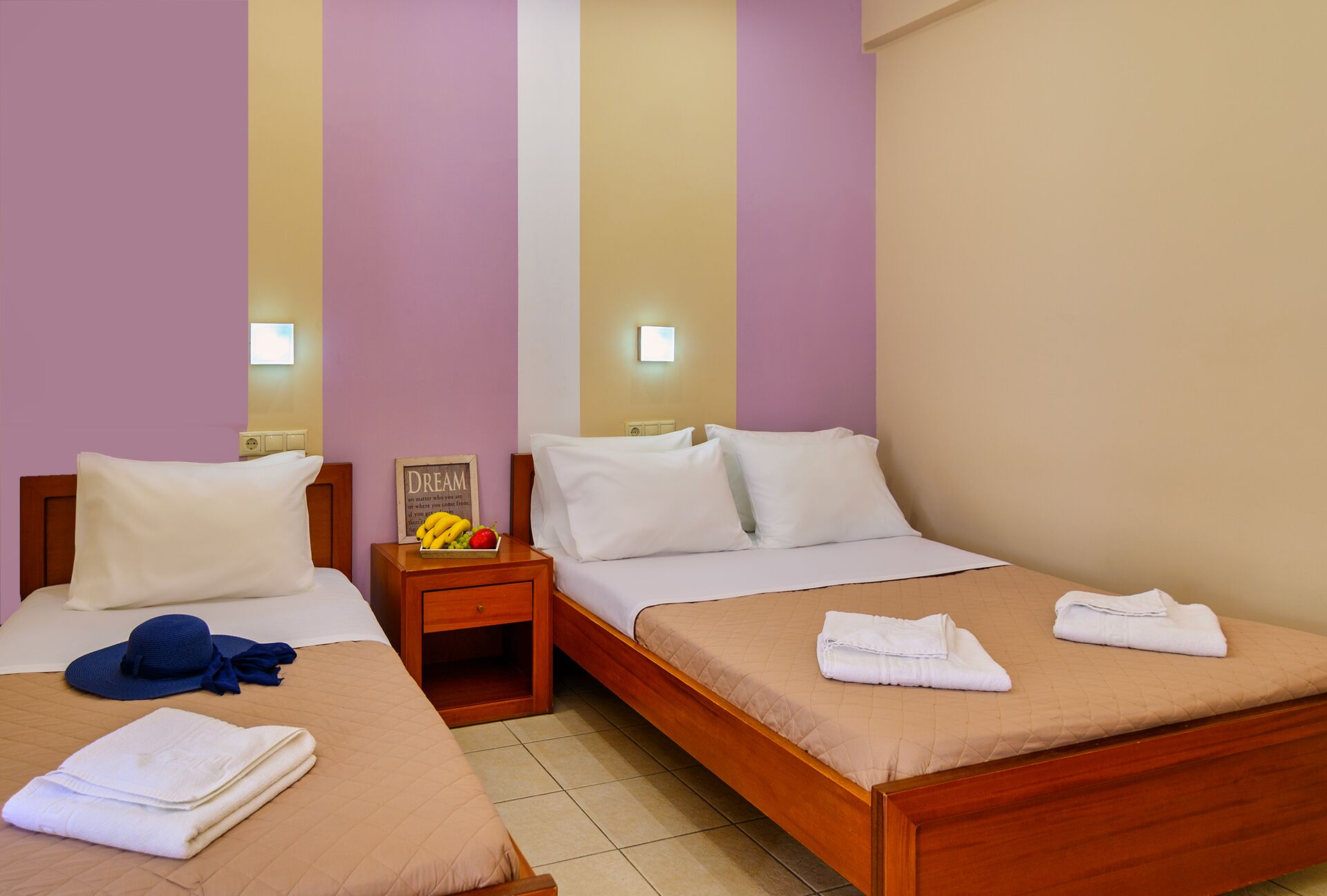 Habitación de hotel con dos camas individuales, una mesita de noche con frutero y una lámpara fijada a la pared.