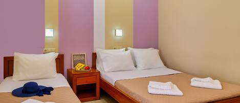 Habitación de hotel con dos camas individuales, una mesita de noche con frutero y una lámpara fijada a la pared.
