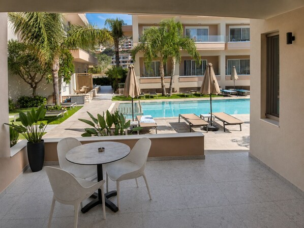 Zona junto a la piscina con sillones reclinables, una mesa y vistas a la piscina y edificios circundantes.