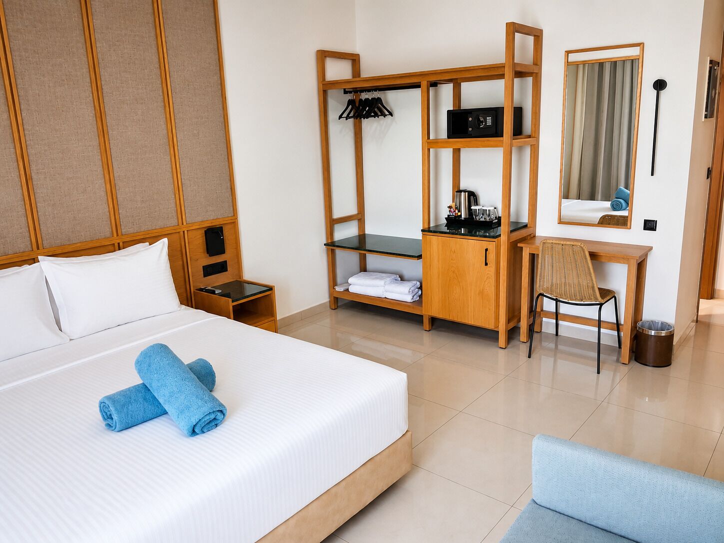 A hotel room with a bed, a desk, a chair, a wardrobe, a mirror, and a trash bin.
