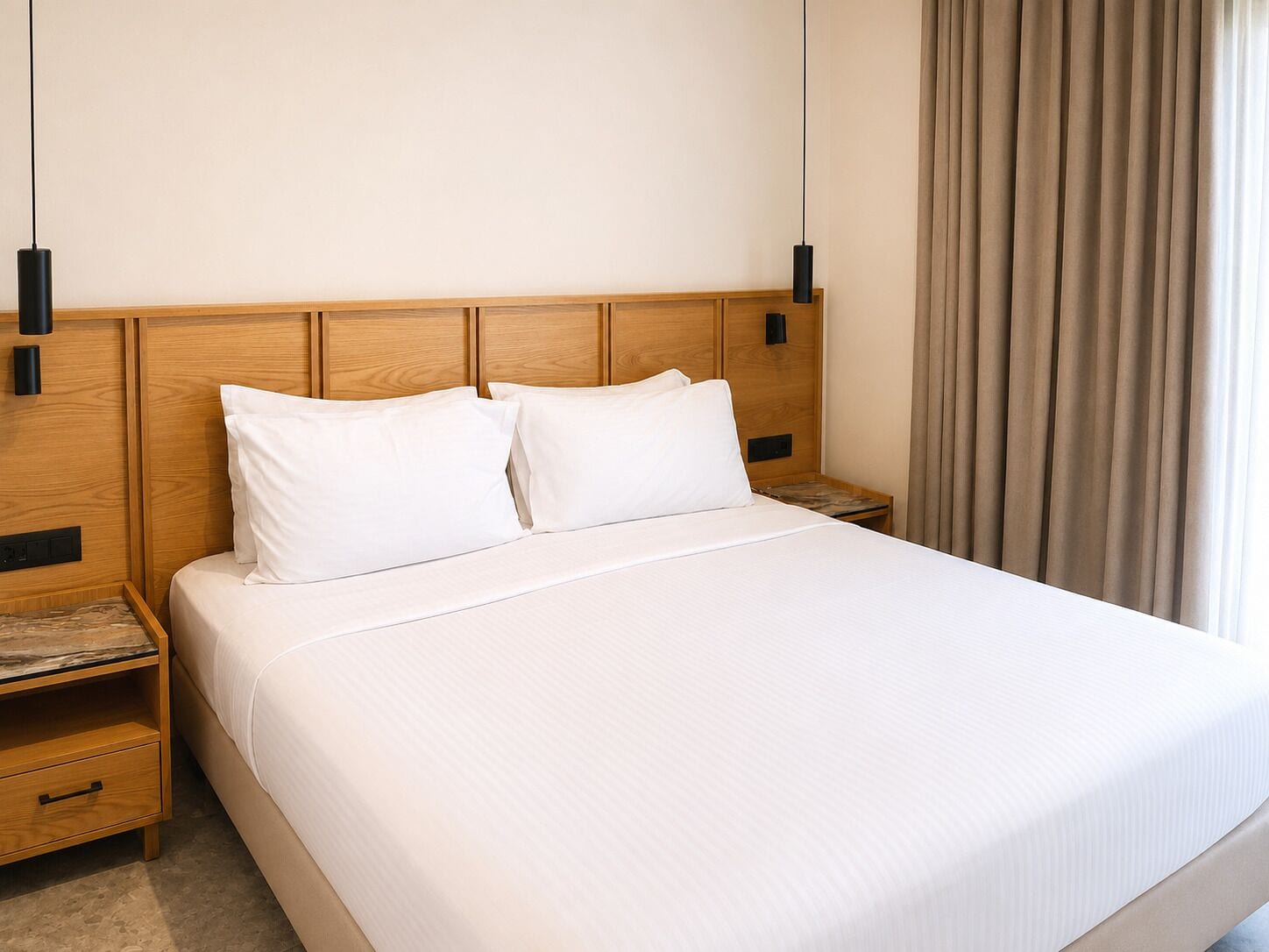 A hotel room with a wooden headboard, two bedside tables, a bed with white linens, and a window with curtains.