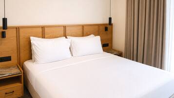 Habitación de hotel con cabecera de madera, dos mesitas de noche, cama con ropa blanca y una ventana con cortinas.