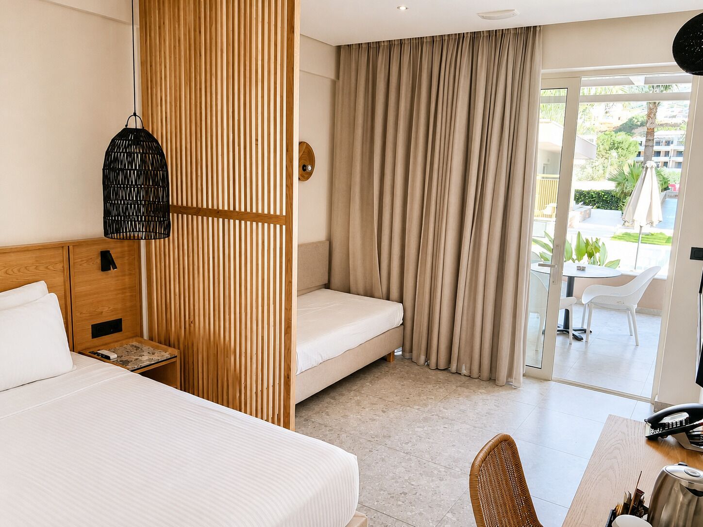 Habitación de hotel con cama, escritorio con teléfono, silla, ventana con cortinas y vista al exterior.