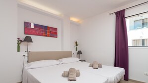 Habitación de hotel con una cama grande, dos mesitas de noche, un cuadro abstracto moderno y vistas al exterior.