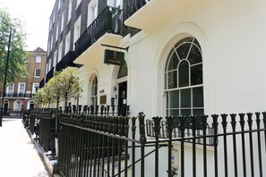 A row of black wrought iron fences with a white building featuring arched windows and a sign above the entrance. - KX Rooms (London)