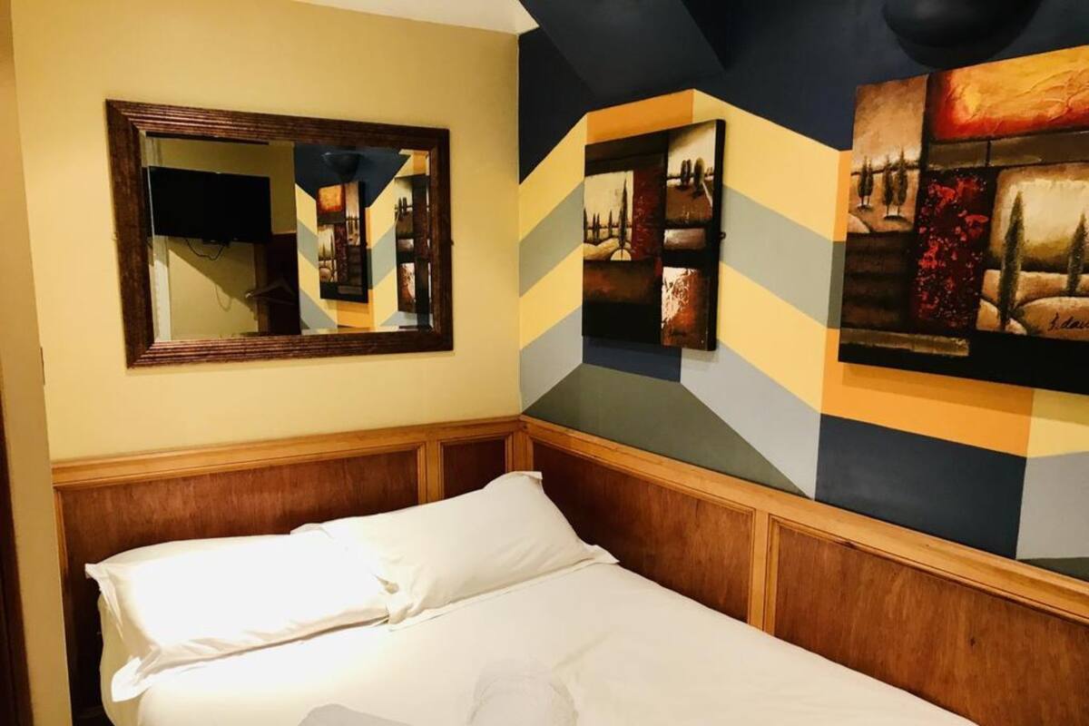 Hotellihuone, jossa on sänky, suuri peili ja kaksi taulua seinällä.