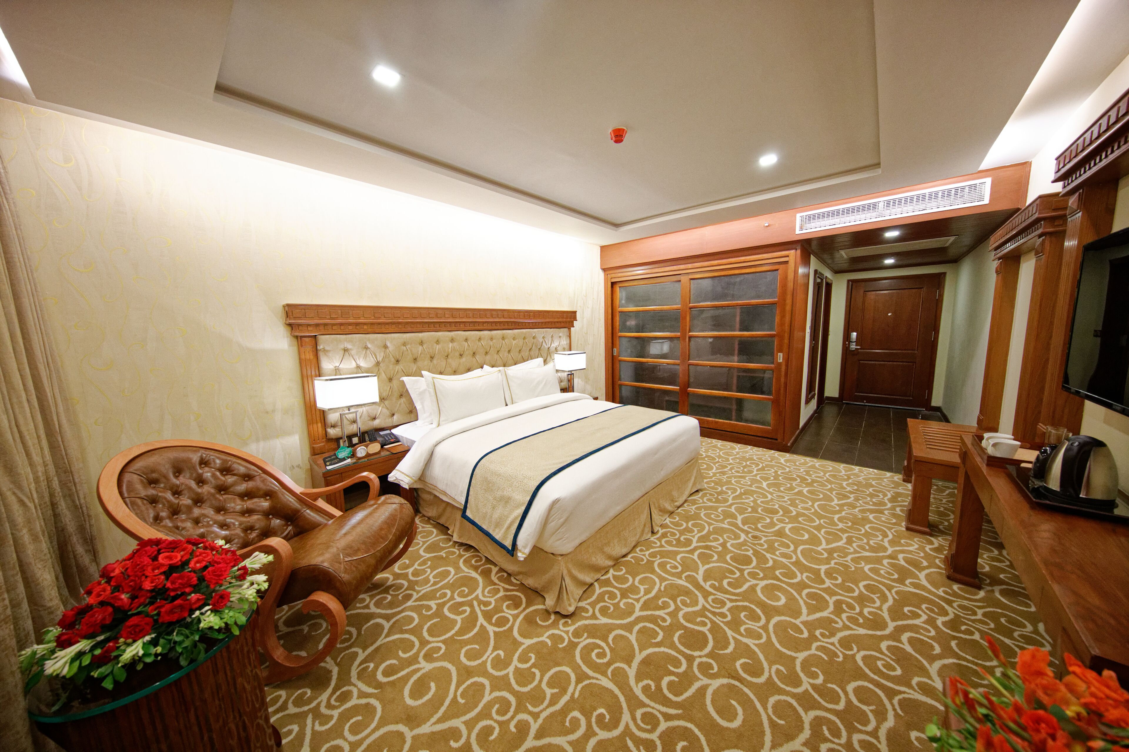 Habitación de hotel con una cama grande, un área de estar con una silla y una mesa, un televisor y un baño con espejo y armario.
