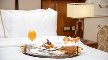 A breakfast tray with toast, a glass of orange juice, and a basket of bread on a bed in a hotel room.