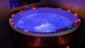 A hot tub with rose petals and candles around its edge, a control panel on the side, and a wooden paneling base. - Royal Swiss Lahore (Lahore)