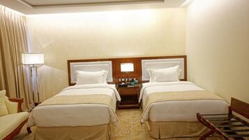 A hotel room with two beds, a nightstand with a lamp, a chair, and a desk.