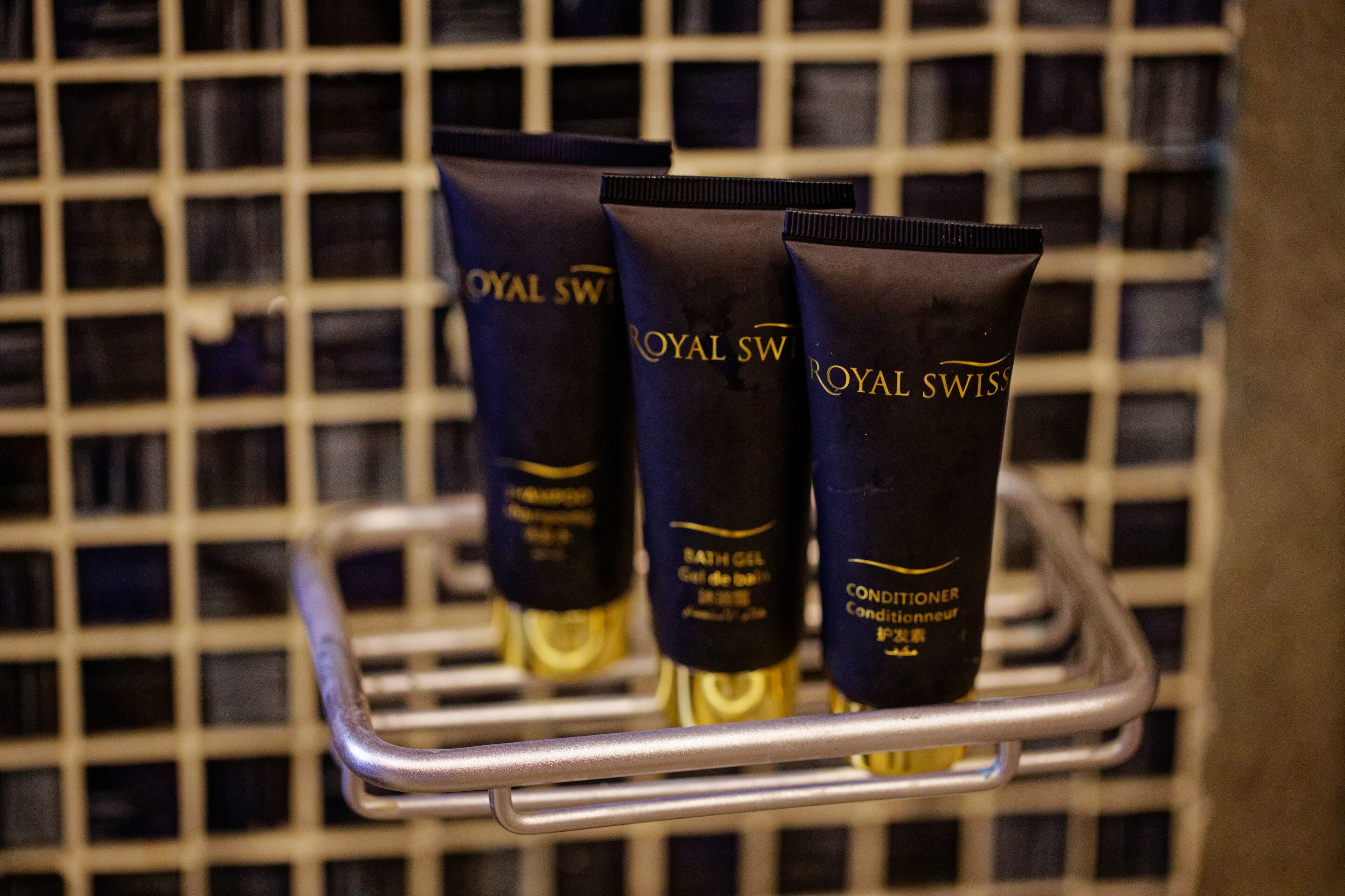Tres tubos de gel de baño Royal Swiss en una cesta metálica, frente a una pared de azulejos.