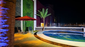 A pool area with a wooden deck, a palm tree, and a red umbrella. - Royal Swiss Lahore (Lahore)