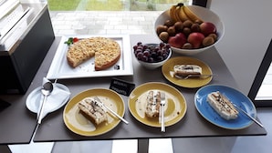 A table with a variety of desserts and fruits, including a pie, cakes, and a bowl of kiwis, apples, and grapes.