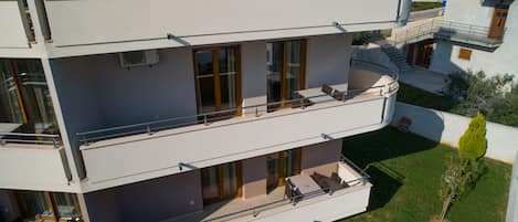 Un edificio residencial de varios pisos con balcones, ventanas grandes y un pequeño jardín.