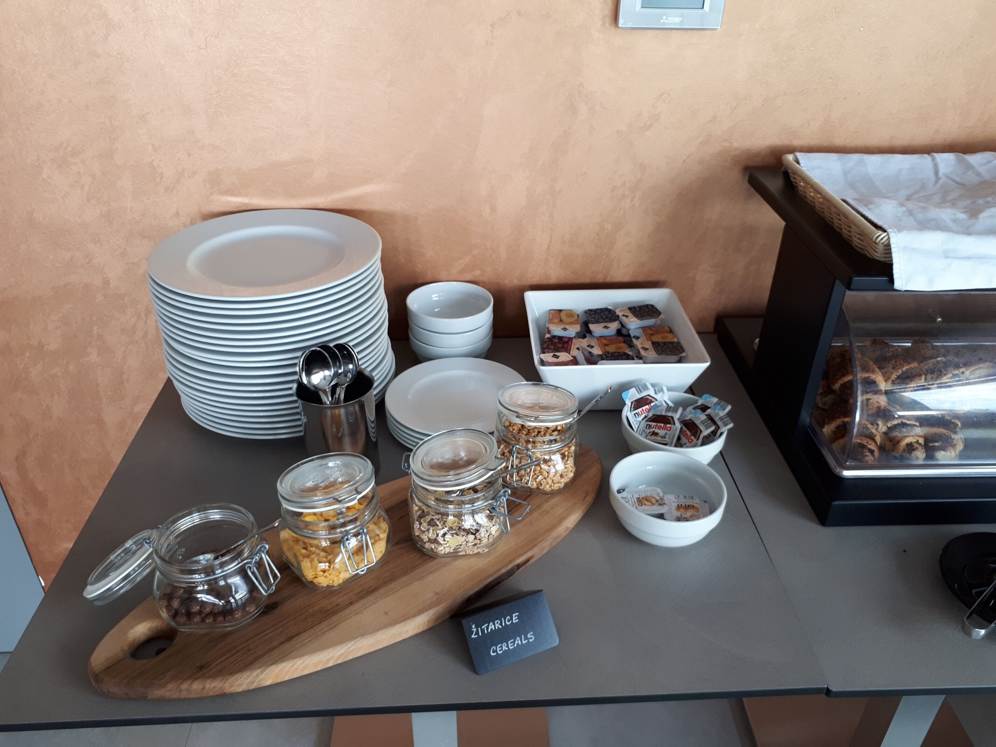A breakfast buffet setup with plates, bowls, and jars of cereals and spreads.