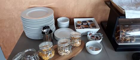 A breakfast buffet setup with plates, bowls, and jars of cereals and spreads.