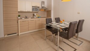 A modern kitchen with a dining area, featuring a glass table, dark chairs, and a built-in microwave.