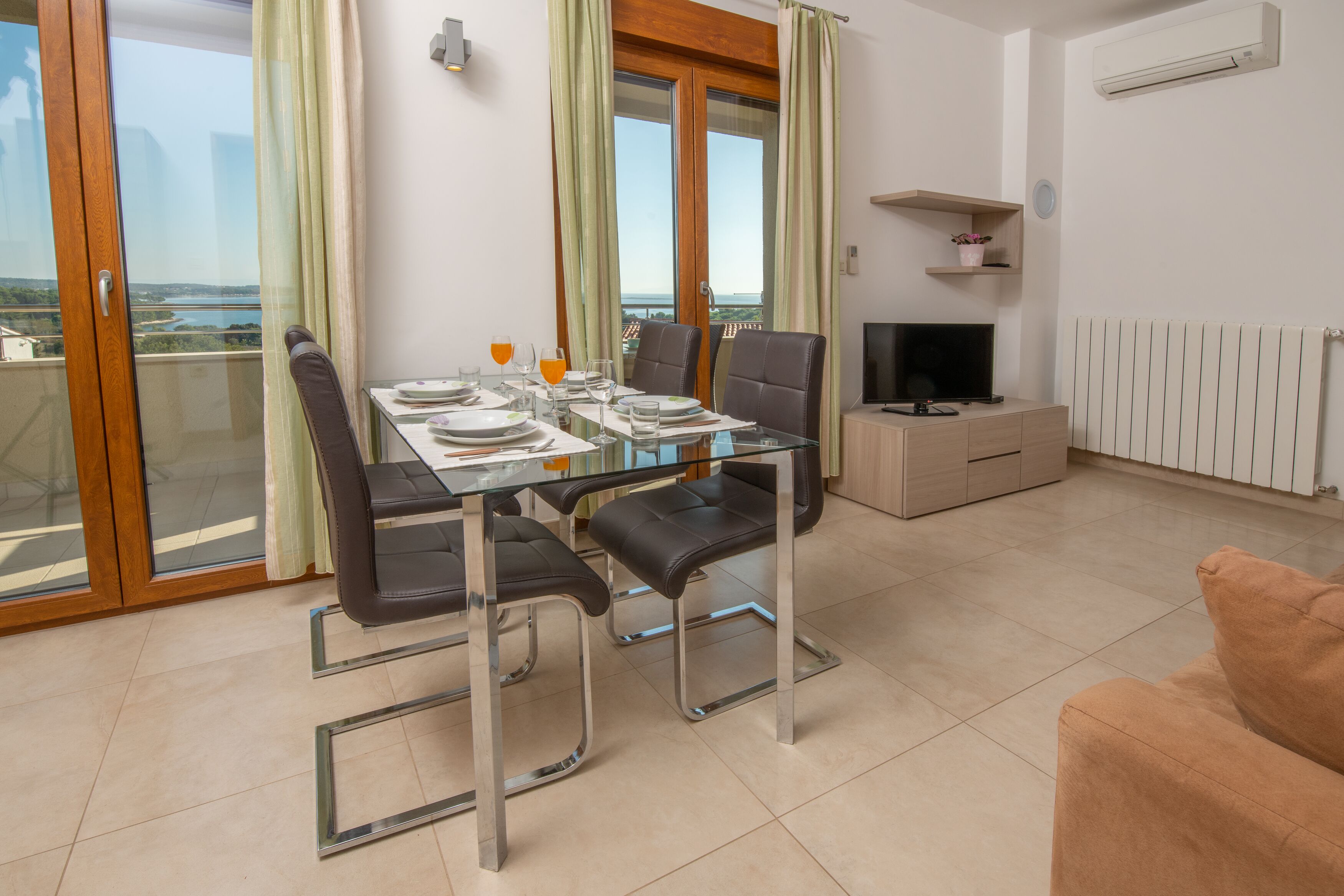 A dining area with a glass table and chairs, a television, and a view of the outdoors.