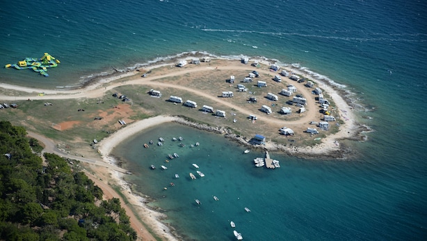 An aerial view of a coastal area with RVs and boats, surrounded by water and greenery.
