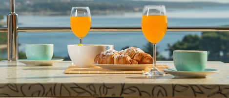 A breakfast setup with croissants, orange juice, and tea cups on a table with a scenic view.