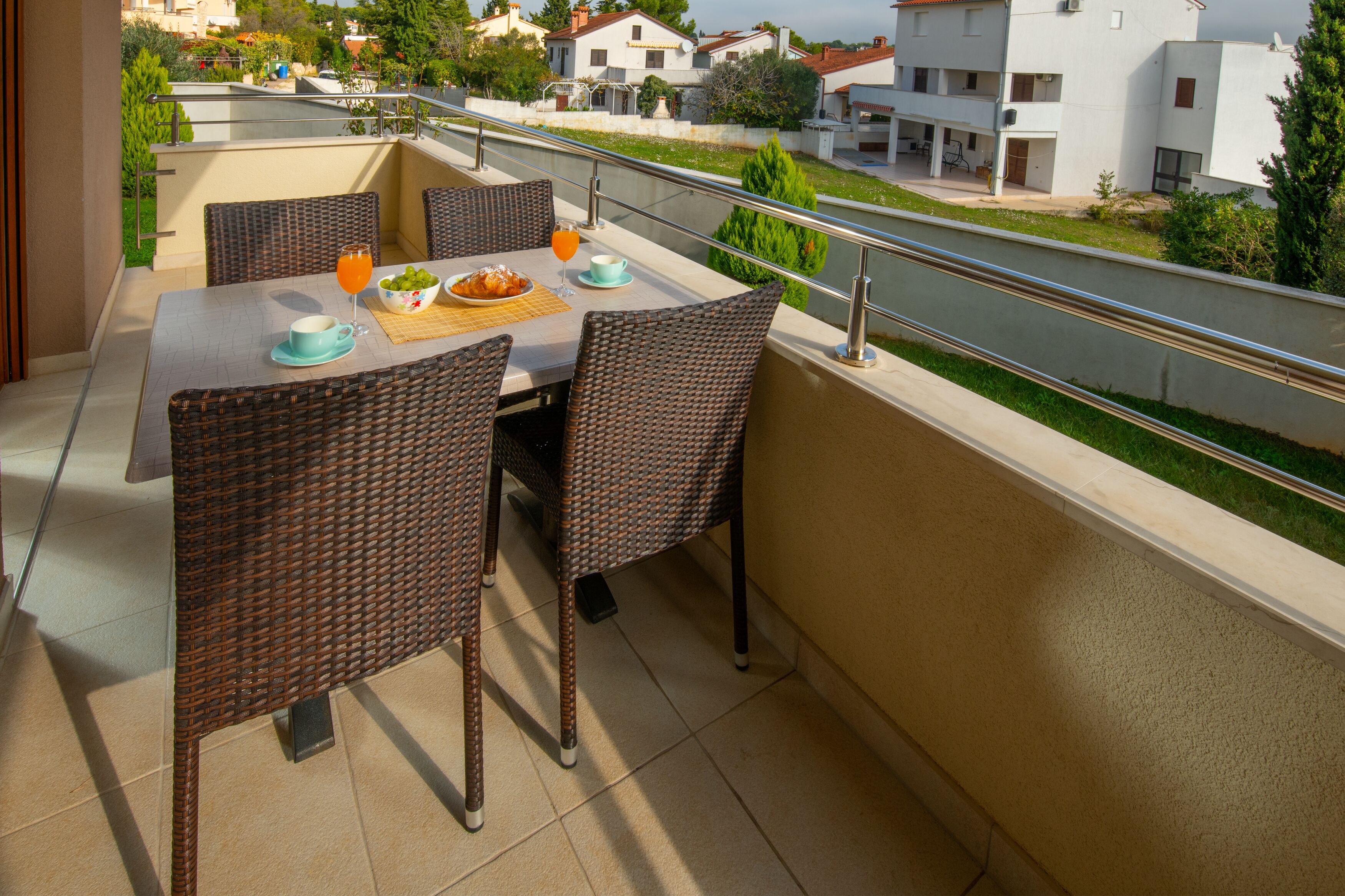 A balcony with wicker furniture, a table set with a bowl of fruit, a glass of orange juice, and a cup.