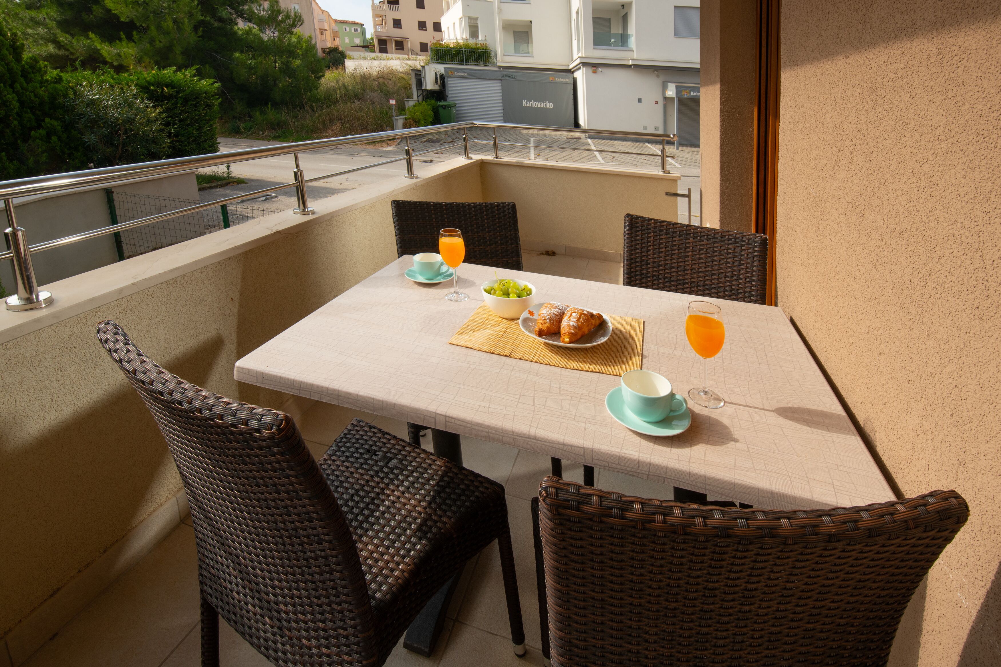En balkon med et bord dækket til morgenmad, fletstole og udsigt over byen.