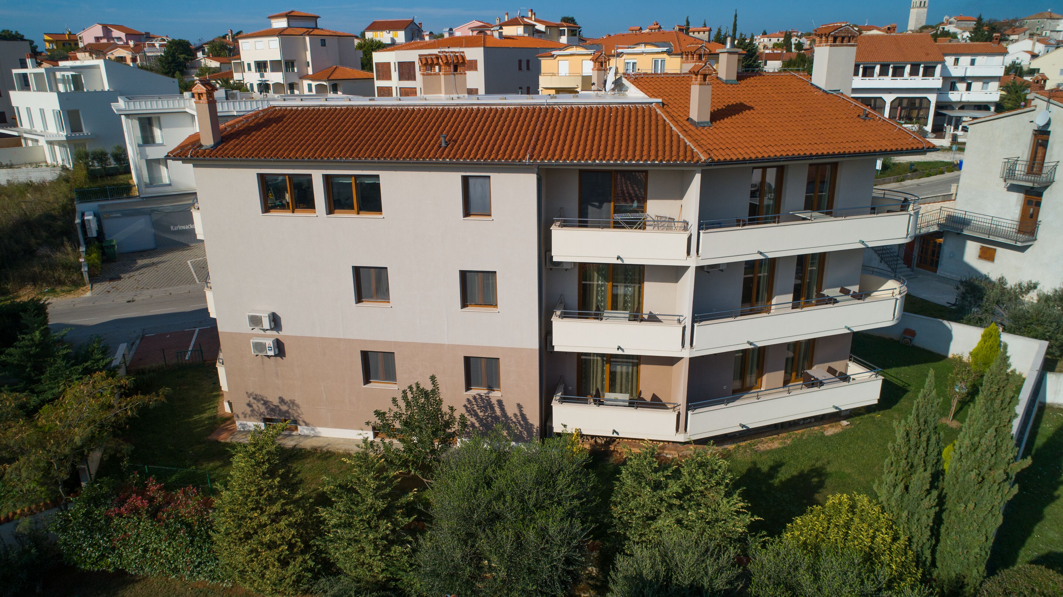 A multi-story building with balconies, a flat roof, and a garden area.