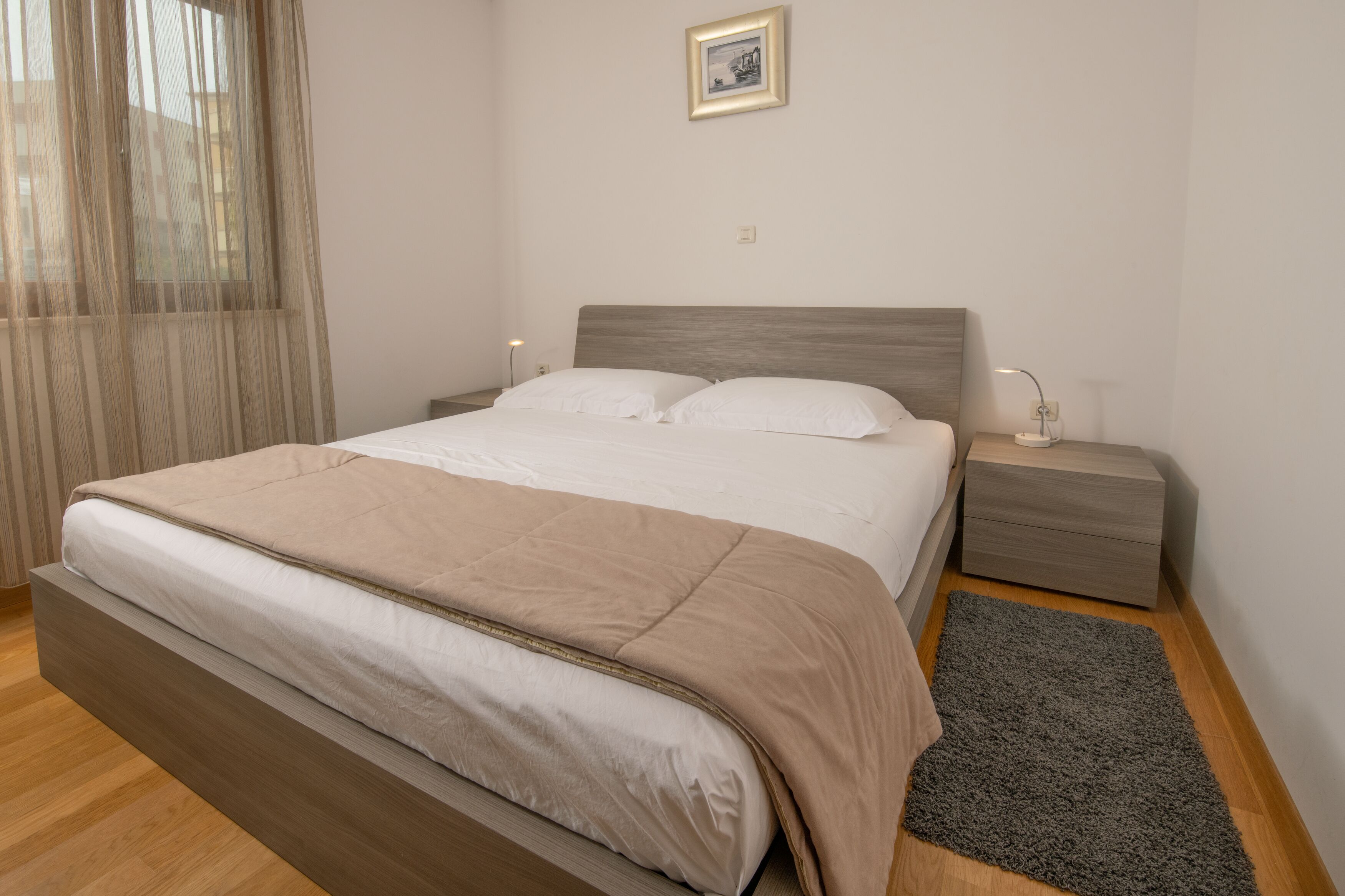 A neatly made bed with a beige blanket, a bedside table with a lamp, and a framed picture on the wall.