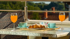 A breakfast setting with croissants, orange juice, and coffee cups on a table with a view of greenery and buildings.