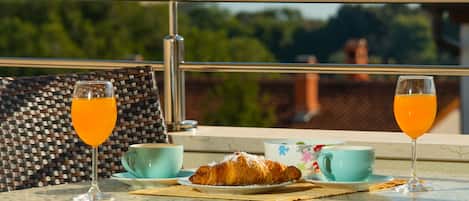 A breakfast setting with croissants, orange juice, and coffee cups on a table with a view of greenery and buildings.