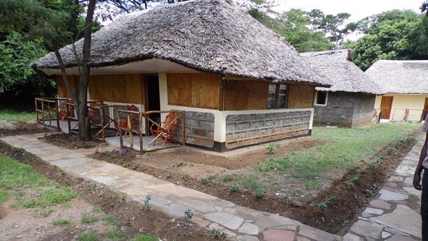 A rustic building with a thatched roof, a porch with wooden chairs, and a stone pathway.