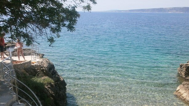 Un paysage côtier avec une eau claire, un promontoire rocheux et un escalier métallique menant à la plage.