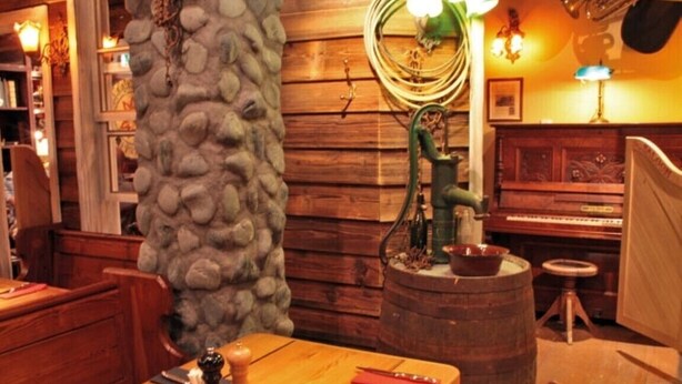 A rustic interior with wooden walls, a stone pillar, a wooden table with cutlery, a piano, and a barrel. - Apartment for a perfect holiday with the family (Greifswald)