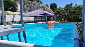 A man in a swimming pool with a purple canopy, surrounded by greenery and a stone wall. - Beautiful house with garden 3 minutes from the beach (Almuñécar)