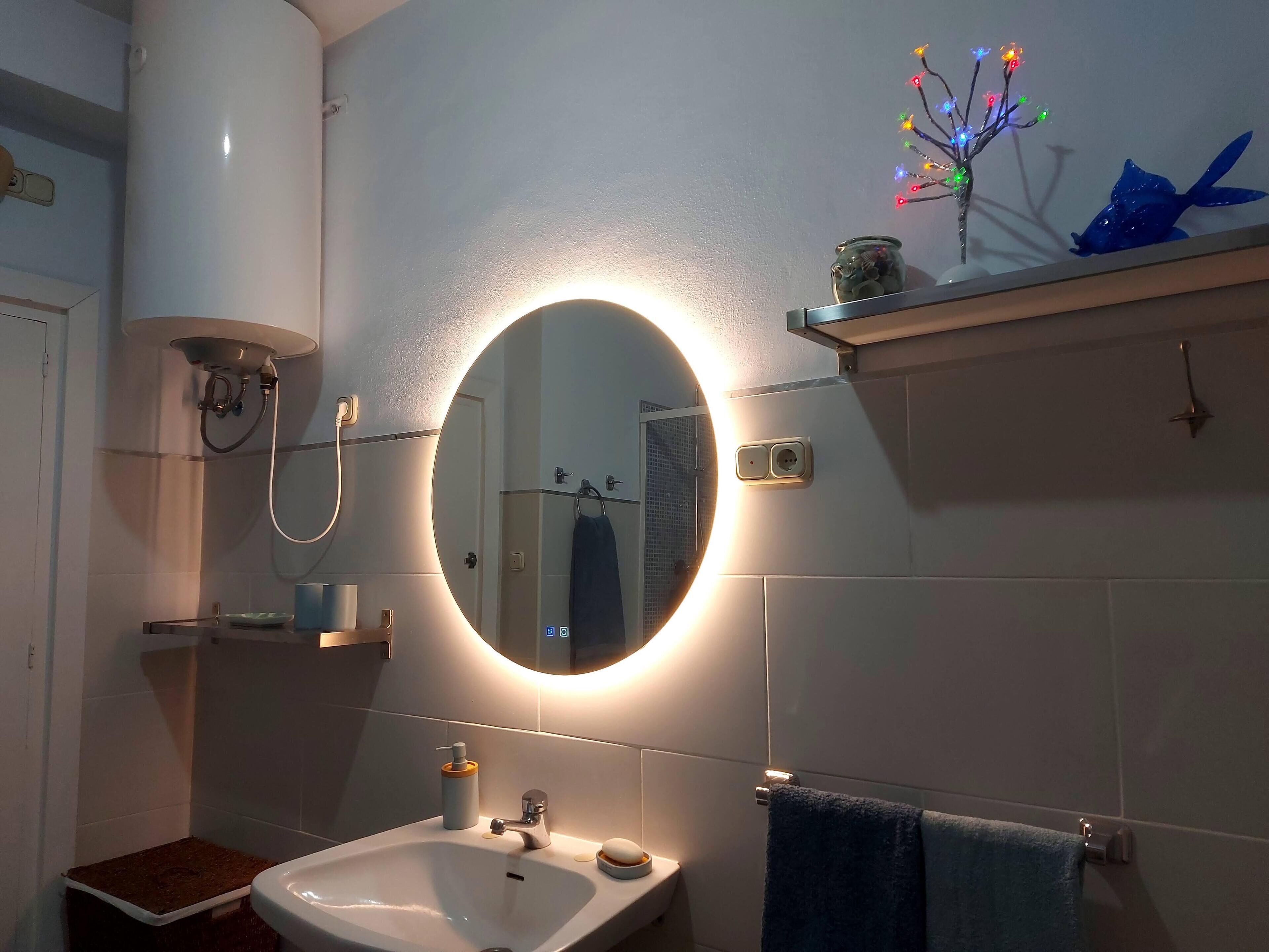 Une salle de bain avec un miroir rond, un lavabo, un porte-serviettes et une étagère ornée d’objets décoratifs.