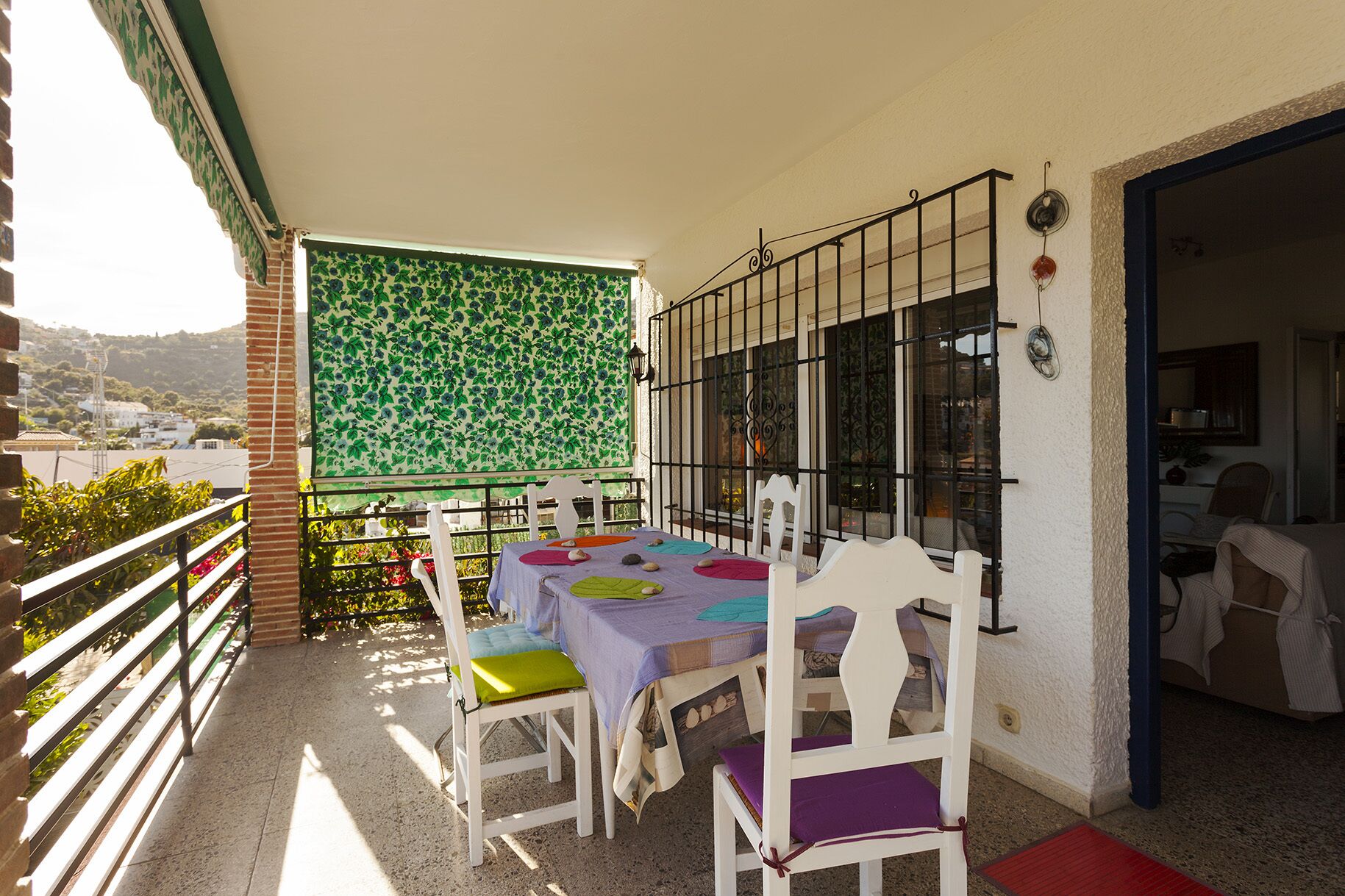 A balcony with a table and chairs, a green patterned wall, and a view of the city.