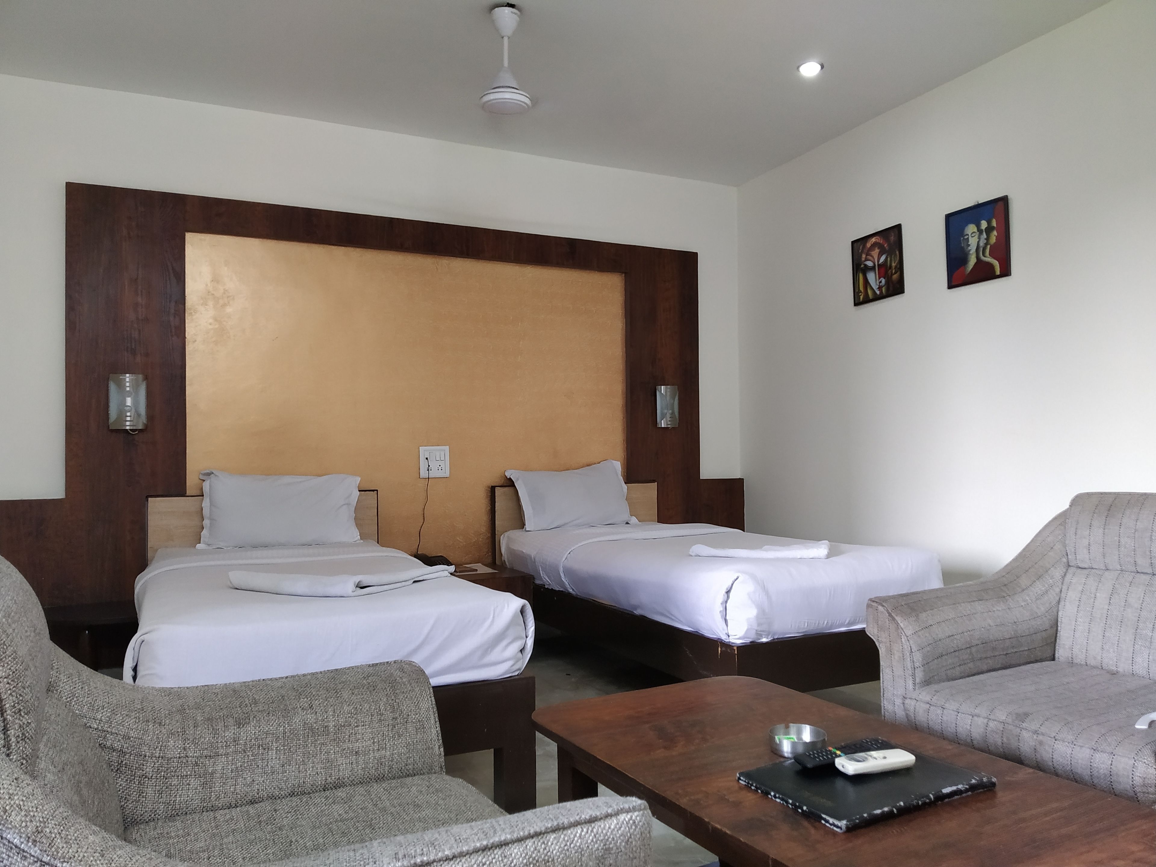 A hotel room with two single beds, a wooden headboard, a small table with a remote control, and a couch.