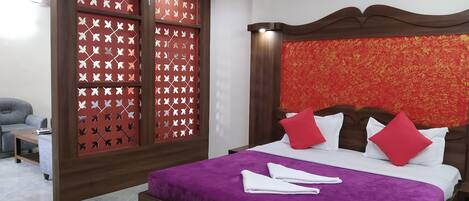 A hotel room with a bed, a wooden headboard, a red patterned partition, and a grey sofa.