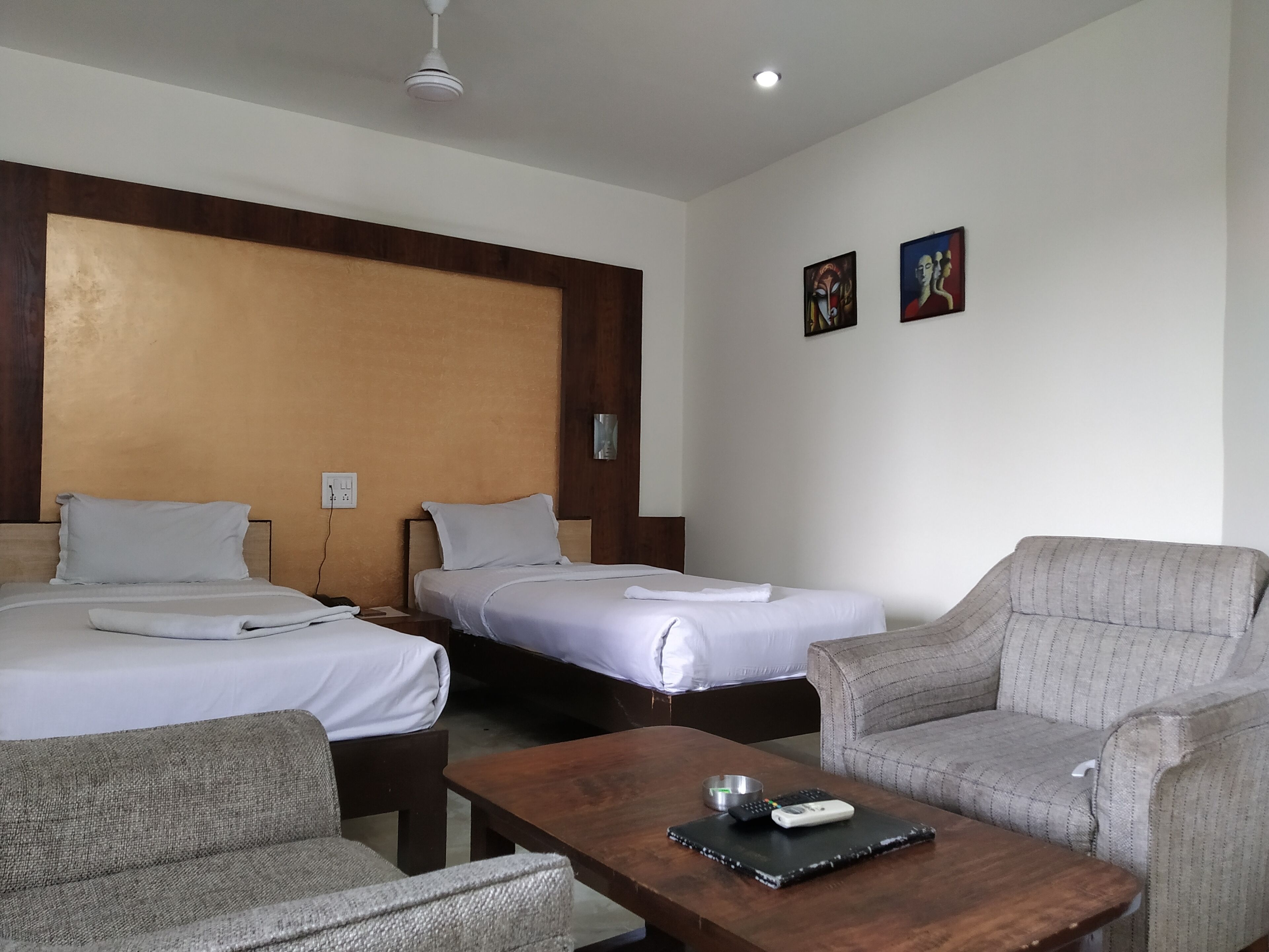 Ein Hotelzimmer mit zwei Einzelbetten, einem Holz-Kopfstück, einem grauen Sofa, einem Holztisch und zwei Bildern an der Wand.