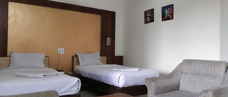Ein Hotelzimmer mit zwei Einzelbetten, einem Holz-Kopfstück, einem grauen Sofa, einem Holztisch und zwei Bildern an der Wand.